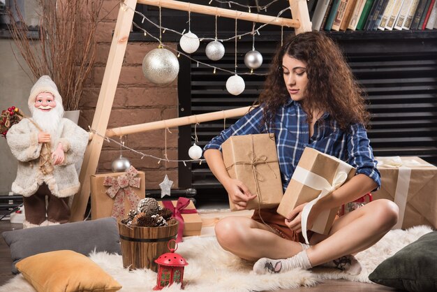 Mujer joven sentada sobre una alfombra mullida con cajas de regalos de Navidad