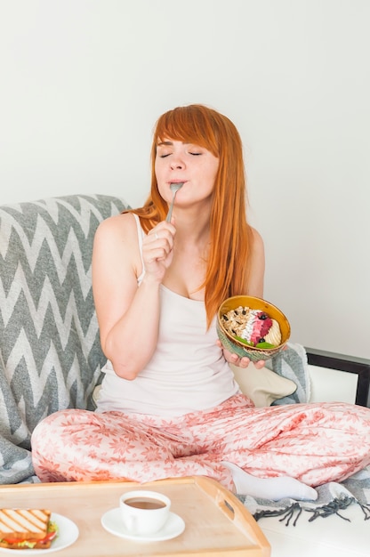 Mujer joven sentada en el sofá comiendo avena granola desayuno