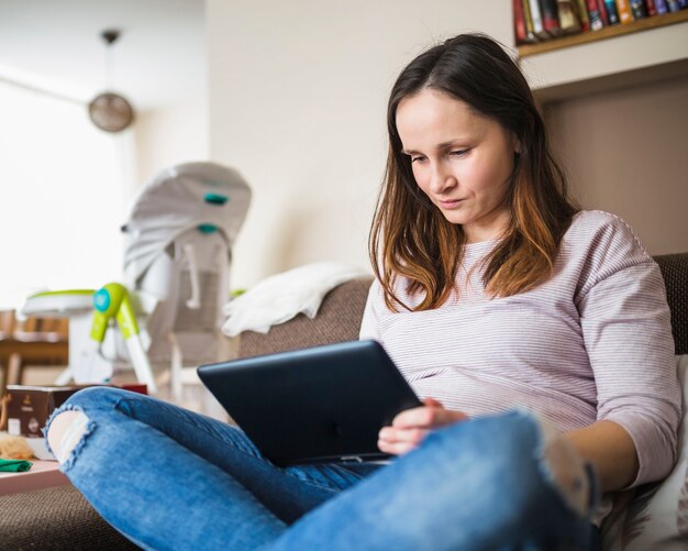 Mujer joven sentada en el sofá con tableta digital