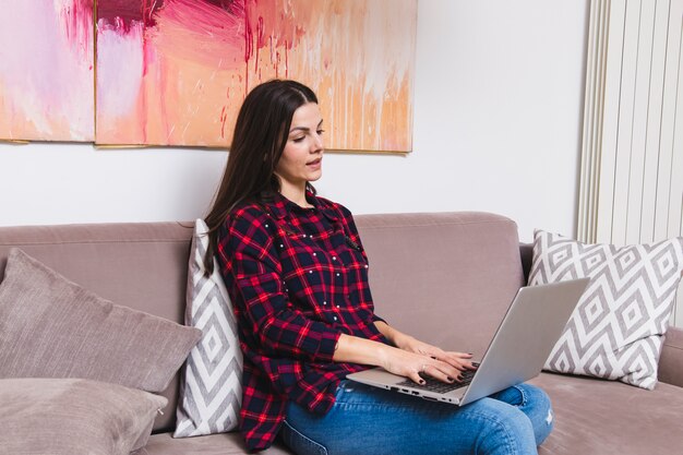 Mujer joven sentada en el sofá usando laptop