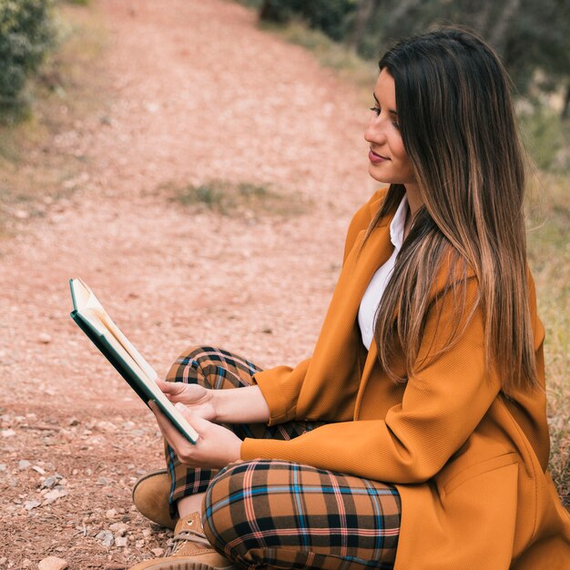 Mujer joven sentada en el suelo con las piernas cruzadas leyendo el libro