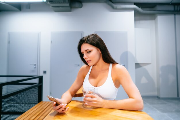 Mujer joven sentada y usando el teléfono inteligente después del entrenamiento