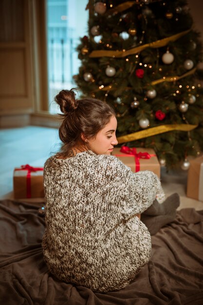 Mujer joven, sentado sobre el piso, cerca, árbol de navidad