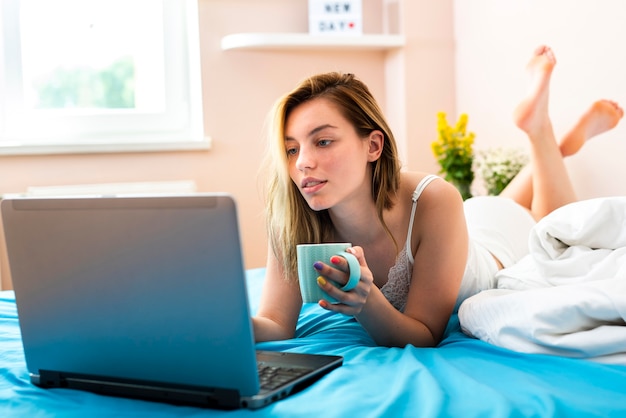 Foto gratuita mujer joven, sentar cama, con, computador portatil