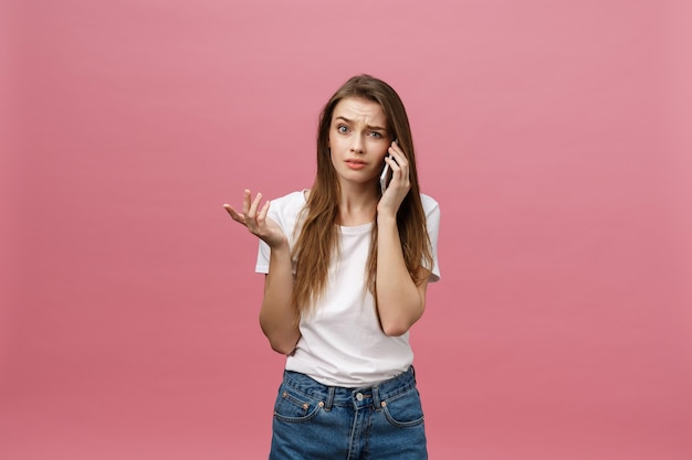 Mujer joven seria hablando por teléfono aislado en rosa Copiar espacio y maqueta de moda