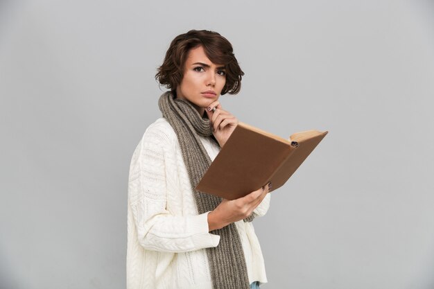 Mujer joven seria con libro de lectura de bufanda.