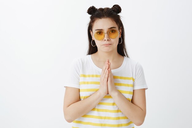 Mujer joven seria preocupada posando con gafas de sol contra la pared blanca