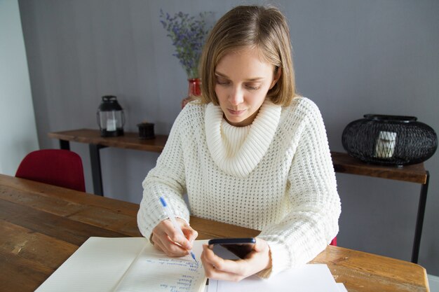 Mujer joven seria que anota tarea en libreta