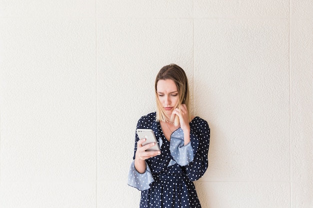 Mujer joven seria que sostiene el teléfono móvil