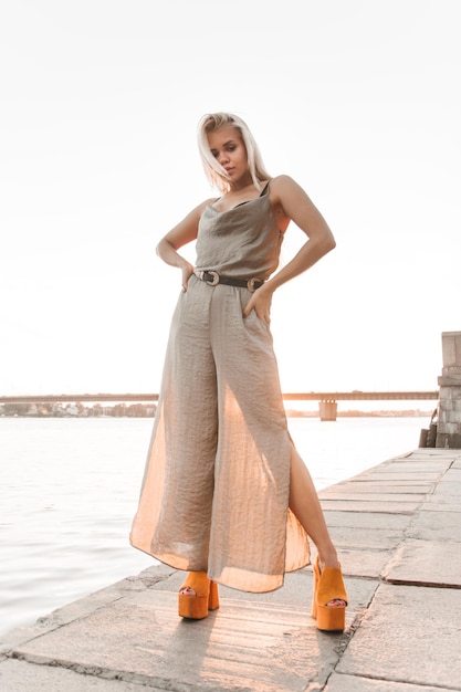 Mujer joven sexy en traje de cuerpo está posando para el fotógrafo en la puesta de sol en la orilla del río.