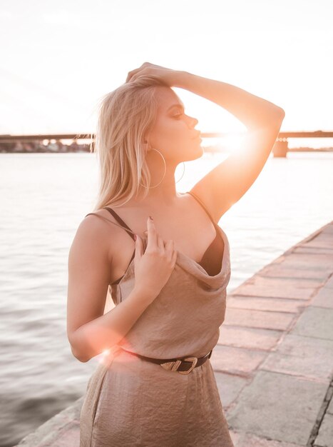 Mujer joven sexy en traje de cuerpo está posando para el fotógrafo en la puesta de sol en la orilla del río.