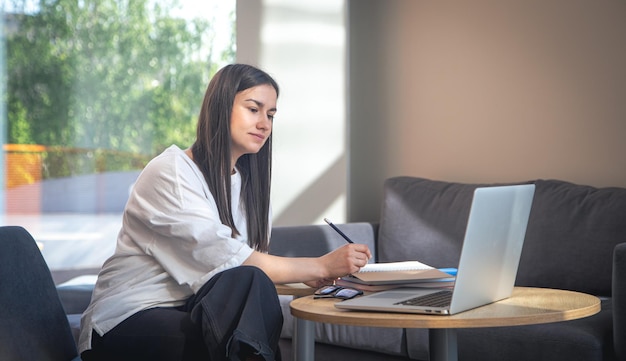 Foto gratuita una mujer joven se sienta frente a una computadora portátil y estudia de forma remota