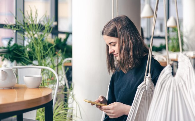 Una mujer joven se sienta en una hamaca colgante y usa un teléfono inteligente