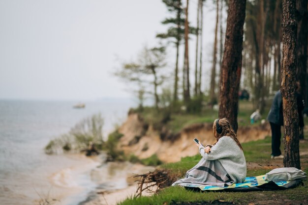 Una mujer joven se sienta en la orilla de un pequeño lago cerca del bosque