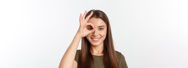 Mujer joven con signo ok en ojo aislado sobre fondo gris