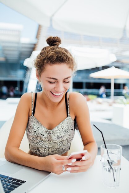 Mujer joven con smartphone en cafetería al aire libre.