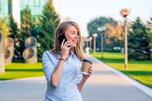 Mujer joven con smartphone caminando en la calle, centro de la ciudad. En el fondo es la calle borrosa, mirando en frente