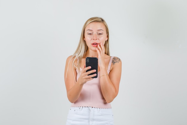 Mujer joven con smartphone en camiseta, minifalda y mirando sorprendido.