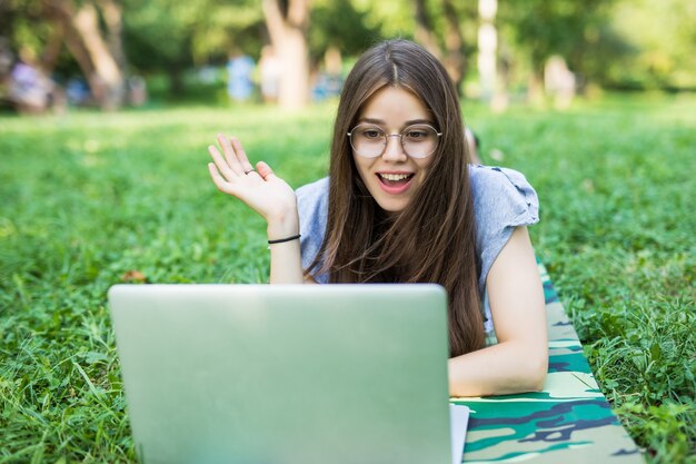 Mujer joven sobre un césped en el parque o jardín usando laptop