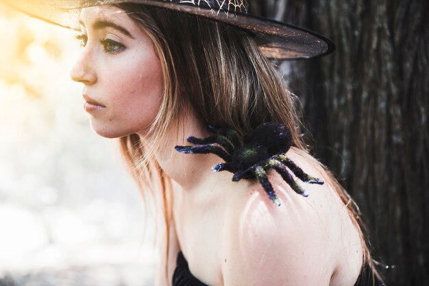 Mujer joven con sombrero con araña decorativa en el hombro mirando a otro lado