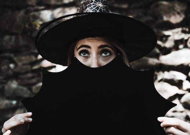 Mujer joven con sombrero de bruja con decoración de Halloween cerca de la cara