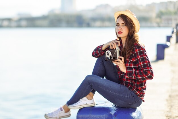 Mujer joven con sombrero y cámara de fotos junto al mar
