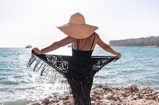 Foto gratuita una mujer joven con sombrero y capa descansa cerca del mar.