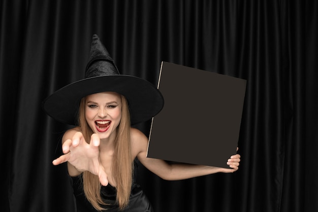 Foto gratuita mujer joven con sombrero como bruja en cortina negra