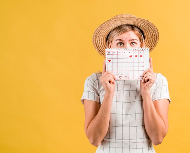 Mujer joven con sombrero cubriendo su rostro con calendario de menstruación