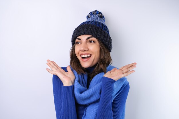 Mujer joven en un sombrero de cuello alto de golf azul y bufanda sobre un fondo blanco alegre de buen humor