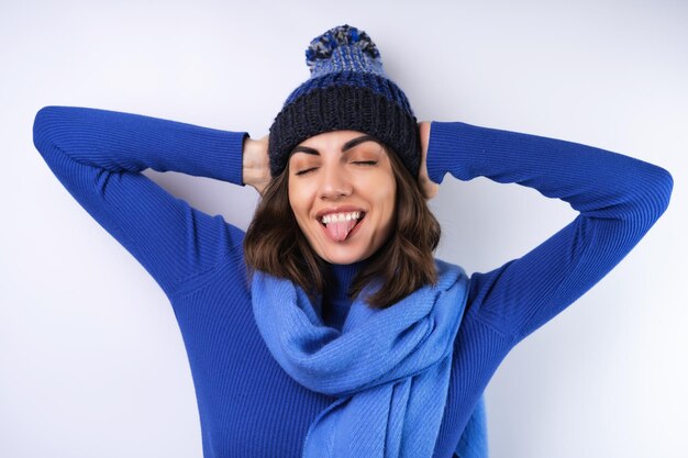 Mujer joven en un sombrero de cuello alto de golf azul y bufanda sobre un fondo blanco alegre de buen humor