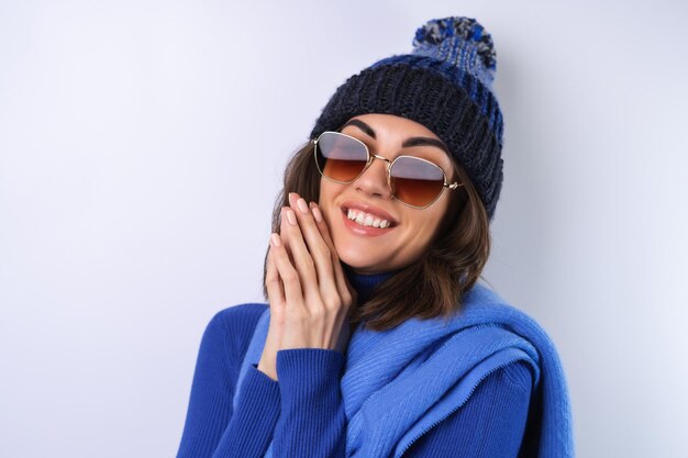 Mujer joven en un sombrero de cuello alto de golf azul y gafas de sol de bufanda sobre un fondo blanco alegre de buen humor