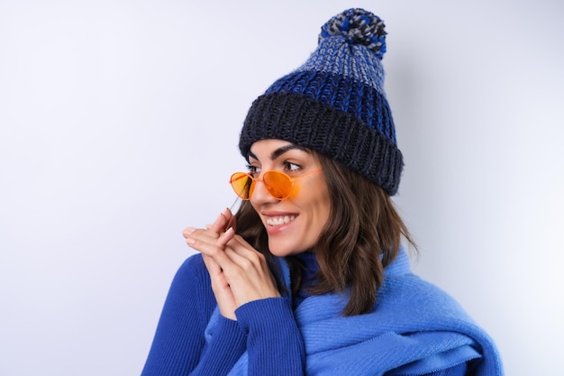 Mujer joven en un sombrero de cuello alto de golf azul y gafas de sol de bufanda sobre un fondo blanco alegre de buen humor