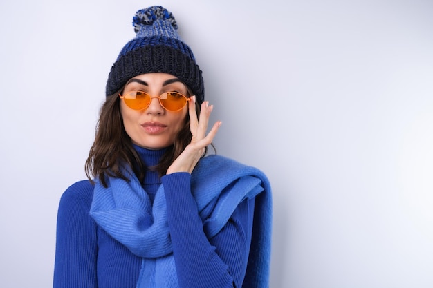 Mujer joven en un sombrero de cuello alto de golf azul y gafas de sol de bufanda sobre un fondo blanco alegre de buen humor