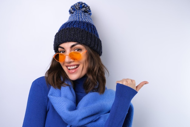 Mujer joven en un sombrero de cuello alto de golf azul y gafas de sol de bufanda sobre un fondo blanco alegre de buen humor