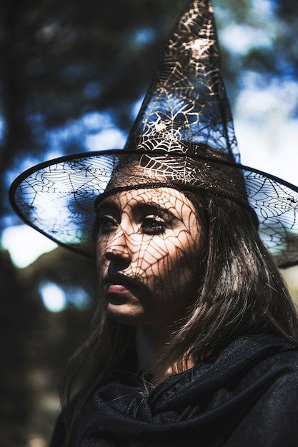 Mujer joven con sombrero de mago y capa mirando lejos en el bosque