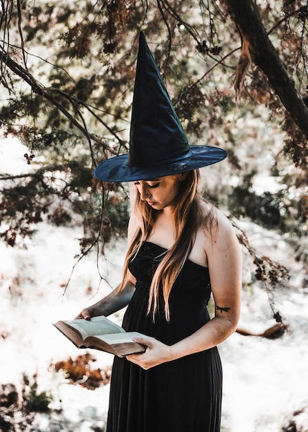 Foto gratuita mujer joven en el sombrero de mago leyendo libro en el bosque