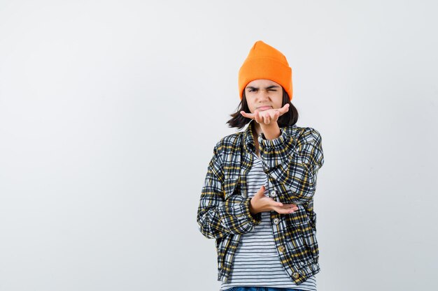 Mujer joven con sombrero naranja y camisa a cuadros pretendiendo tener algo