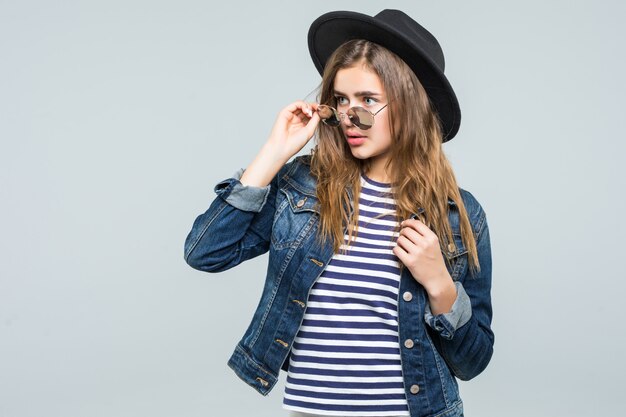 Mujer joven con sombrero negro y gafas de sol aislado sobre fondo blanco.