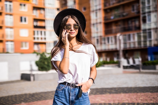 Mujer joven con sombrero negro con teléfono móvil en la calle de la ciudad. chica hablando por teléfono