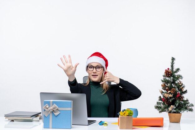 Mujer joven con sombrero de santa claus sentado en una mesa con un árbol de Navidad y un regalo