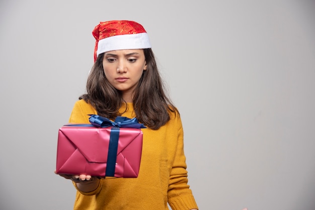 Mujer joven con sombrero de Santa mirando una caja de regalo.