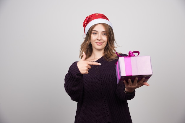 Mujer joven con sombrero de Santa mostrando un presente de caja de regalo.