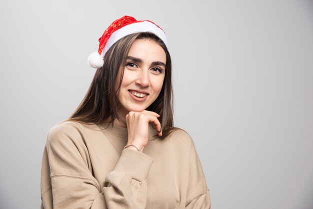 Mujer joven con sombrero de Santa posando tiro de estudio aislado en gris.