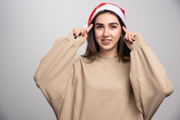 Mujer joven con sombrero de Santa posando tiro de estudio aislado en gris.