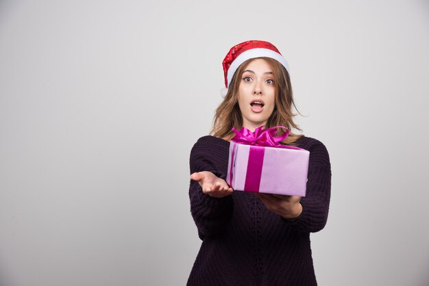 Mujer joven con sombrero de Santa que ofrece una caja de regalo presente.