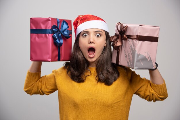 Mujer joven con sombrero de Santa sosteniendo en las manos cajas de regalo.