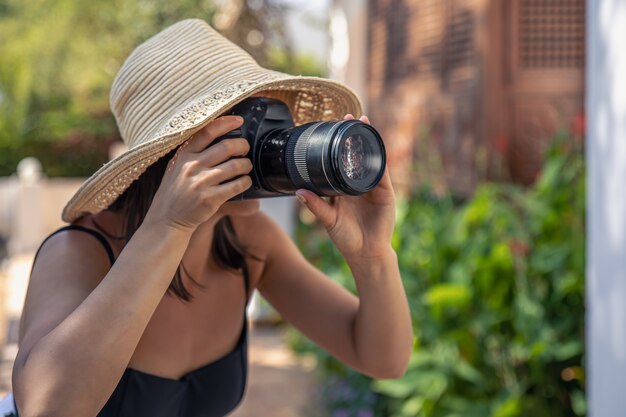 Una mujer joven con sombrero toma fotografías con una cámara SLR profesional en un caluroso día de verano