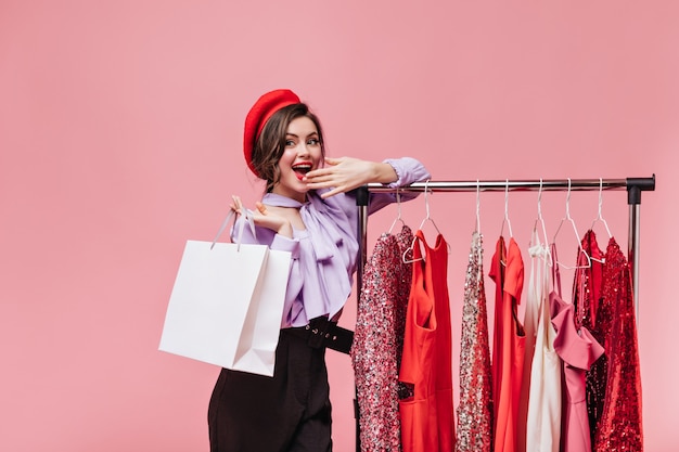 Mujer joven sonríe y se tapa la boca mientras hace compras. Dama de boina posa cerca del stand con disfraces.