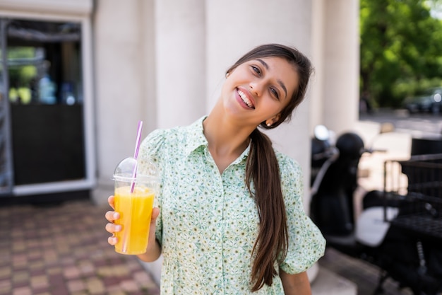 Mujer joven sonriendo y bebiendo cócteles con hielo en vaso de plástico con paja